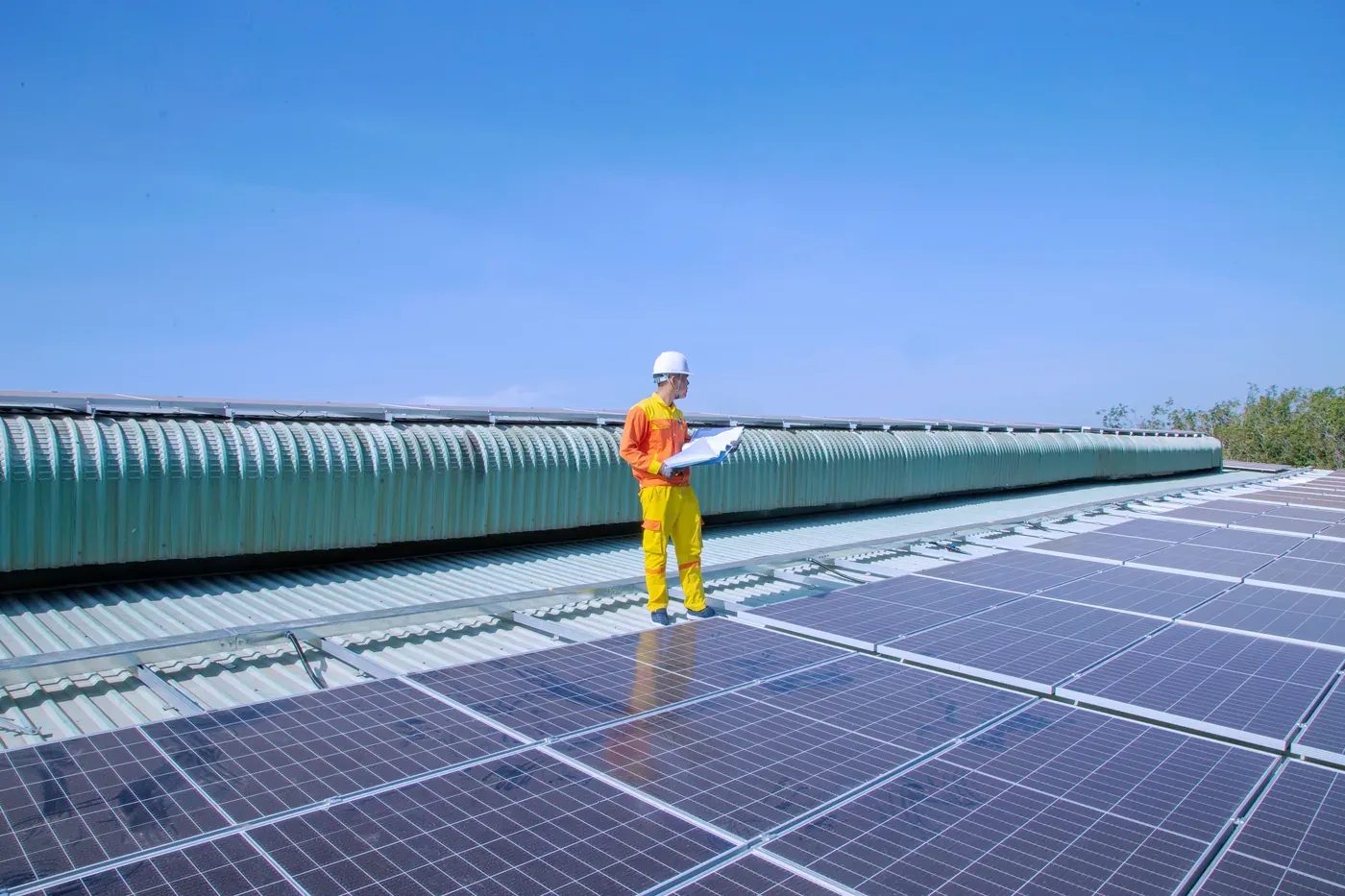 Tecnico con casco e progetto in mano su una copertura industriale con impianto fotovoltaico